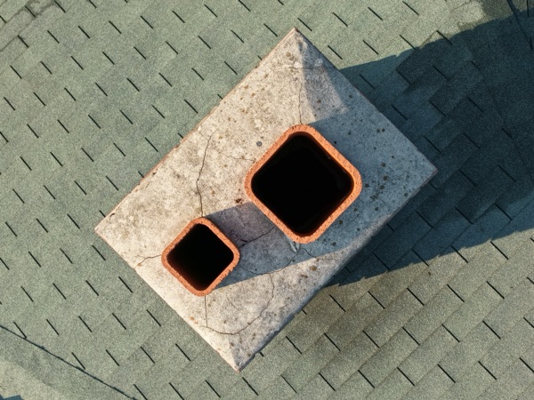 Telephoto close-up of a chimney cap on the pavilion roof, showing flue openings and hairline cracks in the concrete crown