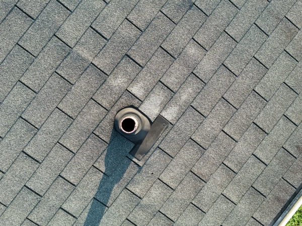 Telephoto close-up of a plumbing vent boot and surrounding asphalt shingle pattern on the pavilion roof